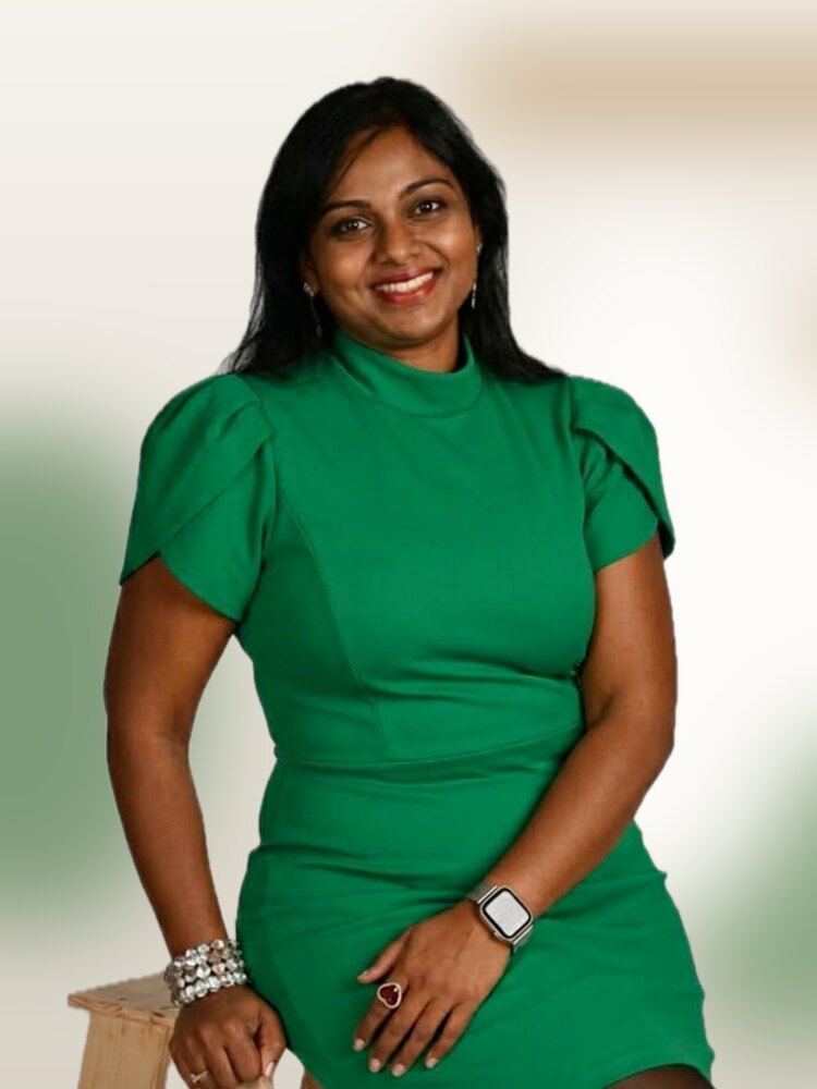 Ramya Sriramulu, seated on a wooden stool in a green dress